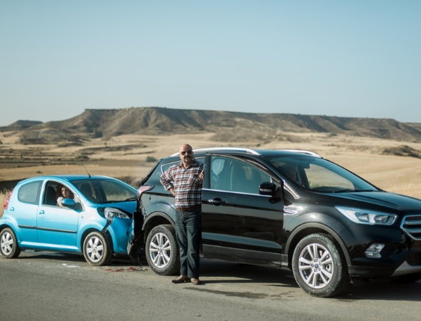 A man standing next to a blue suv in the desert. | The White Leaf 
