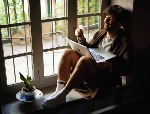 A man sitting on a window sill with a laptop. | The White Leaf 