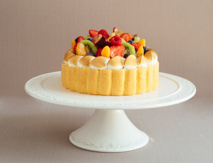 A cake with fruit on top of a cake stand. | The White Leaf 