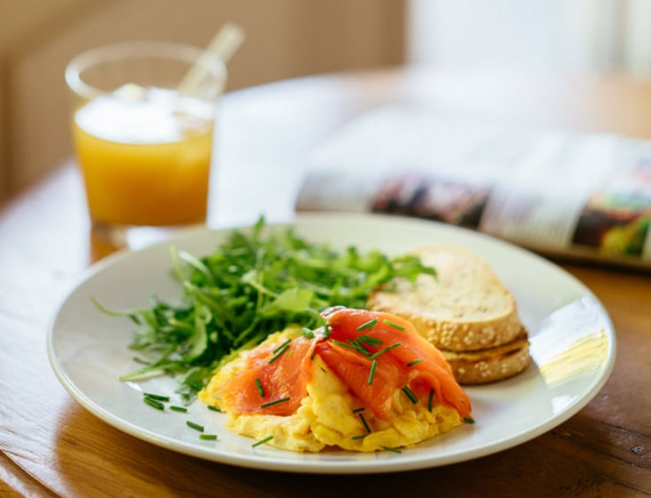 A plate of scrambled eggs with smoked salmon and a glass of orange juice. | The White Leaf 