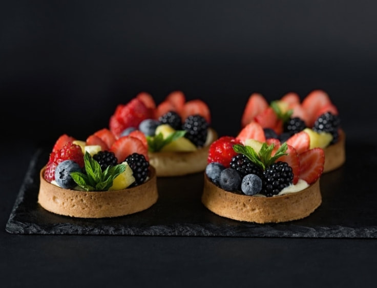 Four tarts with berries and mint on a black background. | The White Leaf 