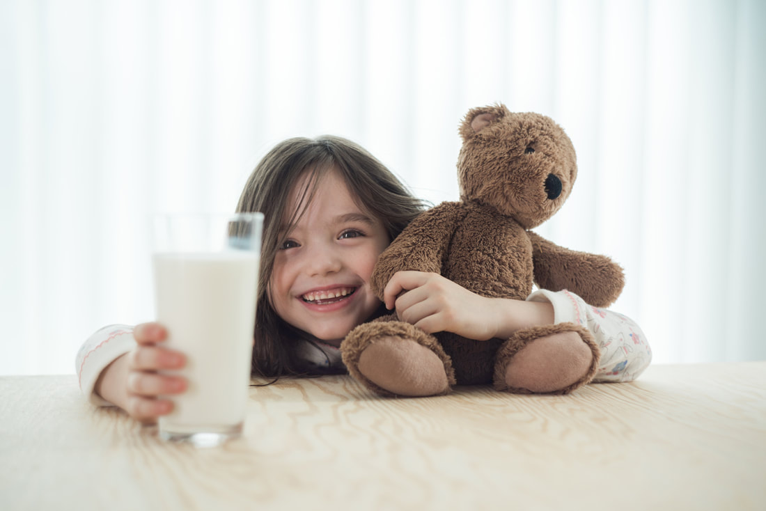 A girl holding a teddy bear and a glass of milk. | The White Leaf 
