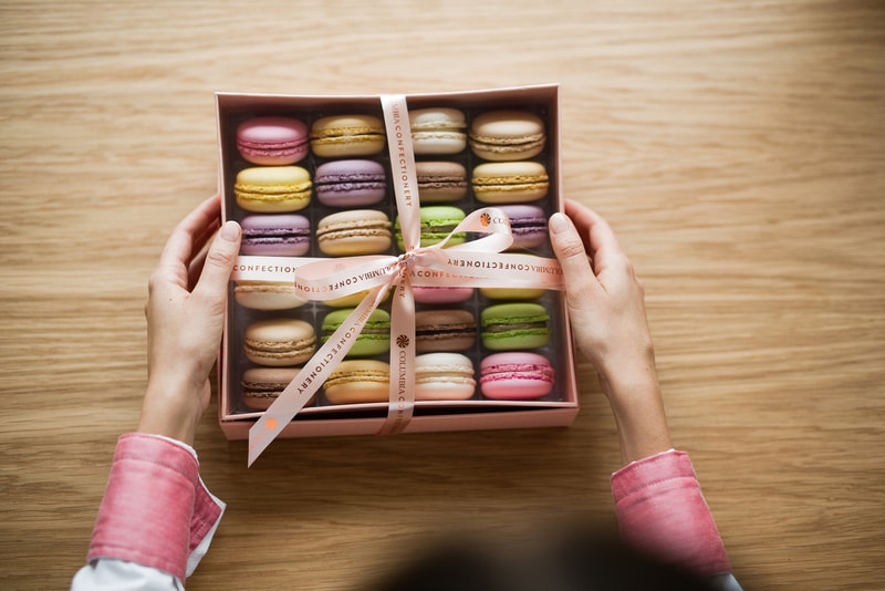 a lady holding a box of macaroons with many colours
