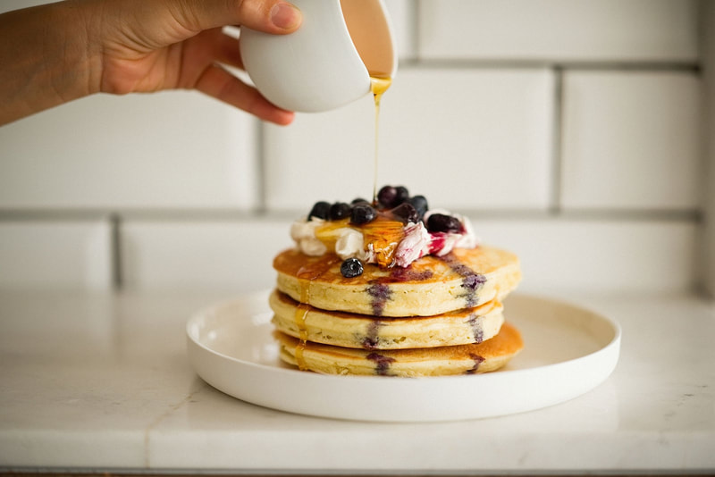 pancakes with fruit ontop and someone pouring honey onto the pancakes