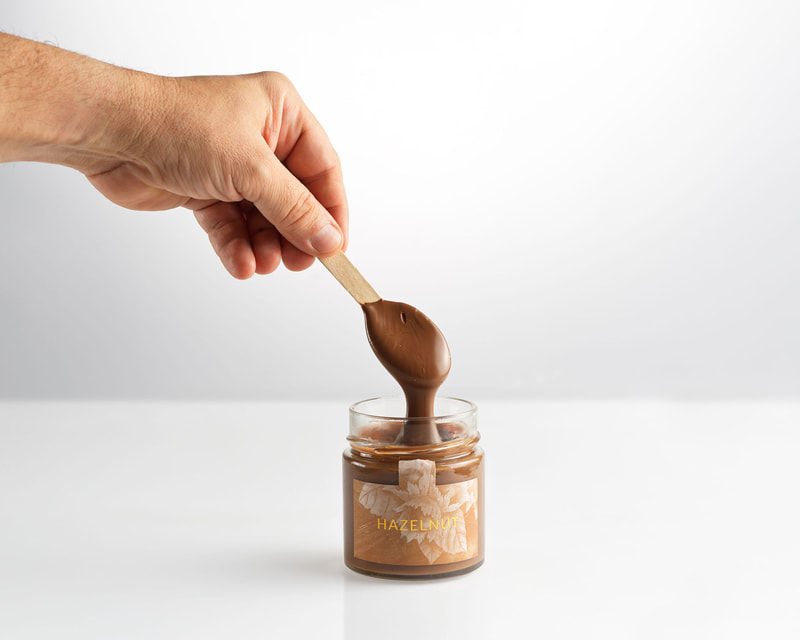 man holding a wooden spoon dipped in a jar of hazelnut chocolate 