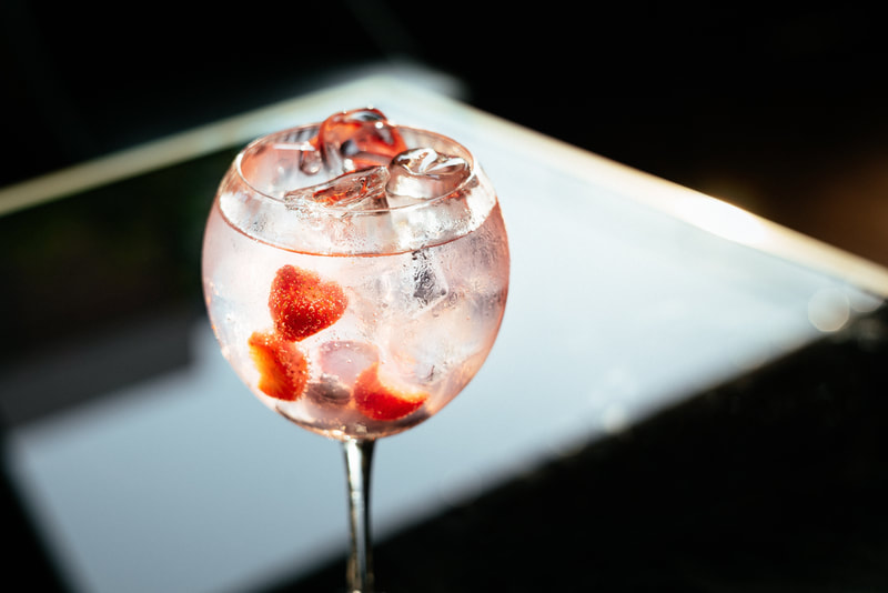 gun and tonic with frozen strawberries and ice in a wine glass