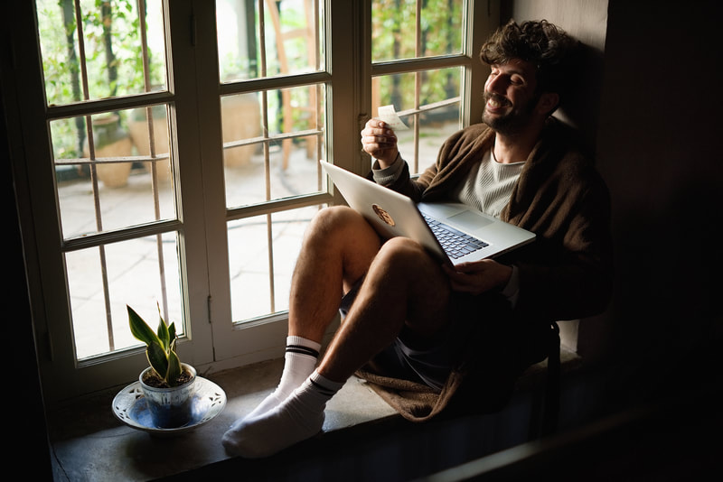 A man sitting on a window sill with a laptop. | The White Leaf 